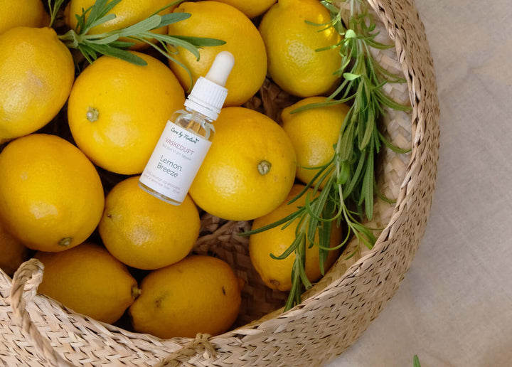 Care by Nature naturlig vaskeduft Lemon Breeze i klar glasflakon med pipette der ligger i en flettet kurv med citroner og frisk rosmarin