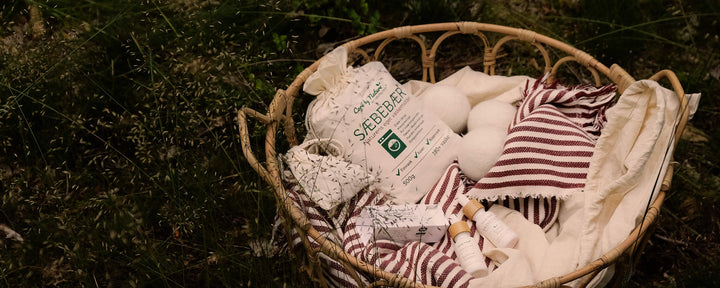  Care by nature sæbebær er et skånsomt og naturligt vaskemiddel af 100% rene naturlige bærskaller (vaskebær) der vasker tøjet rent. Her ses care by nature sæbebær i vasketøjskurv med tæpper og sengetøj på eng