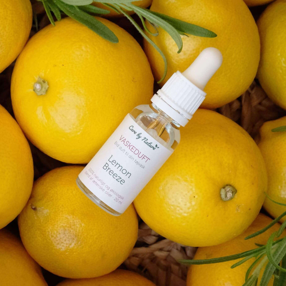 care by nature vaskeduft lemon breeze i klar glasflaske ovenpå citroner og rosmarin i flettet kurv