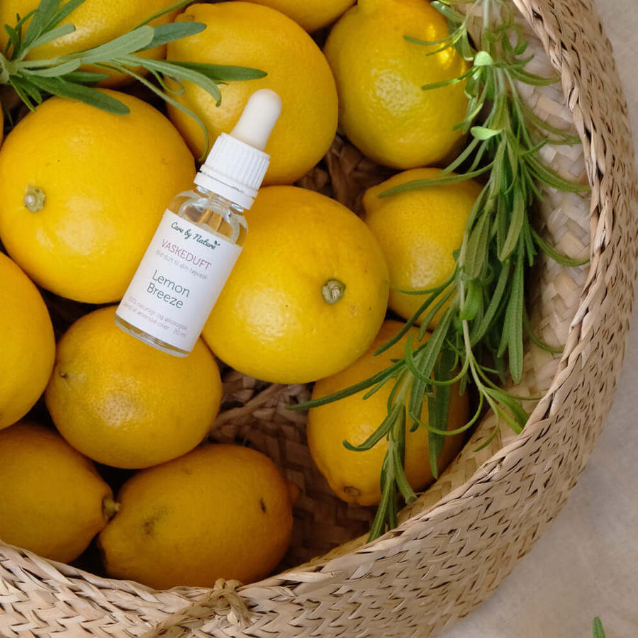 Care by Nature naturlig vaskeduft Lemon Breeze i klar glasflakon med pipette der ligger i en flettet kurv med citroner og frisk rosmarin